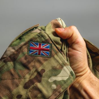 Close-up of a hand holding a UK Armed Forces camouflage uniform with Union Jack patch